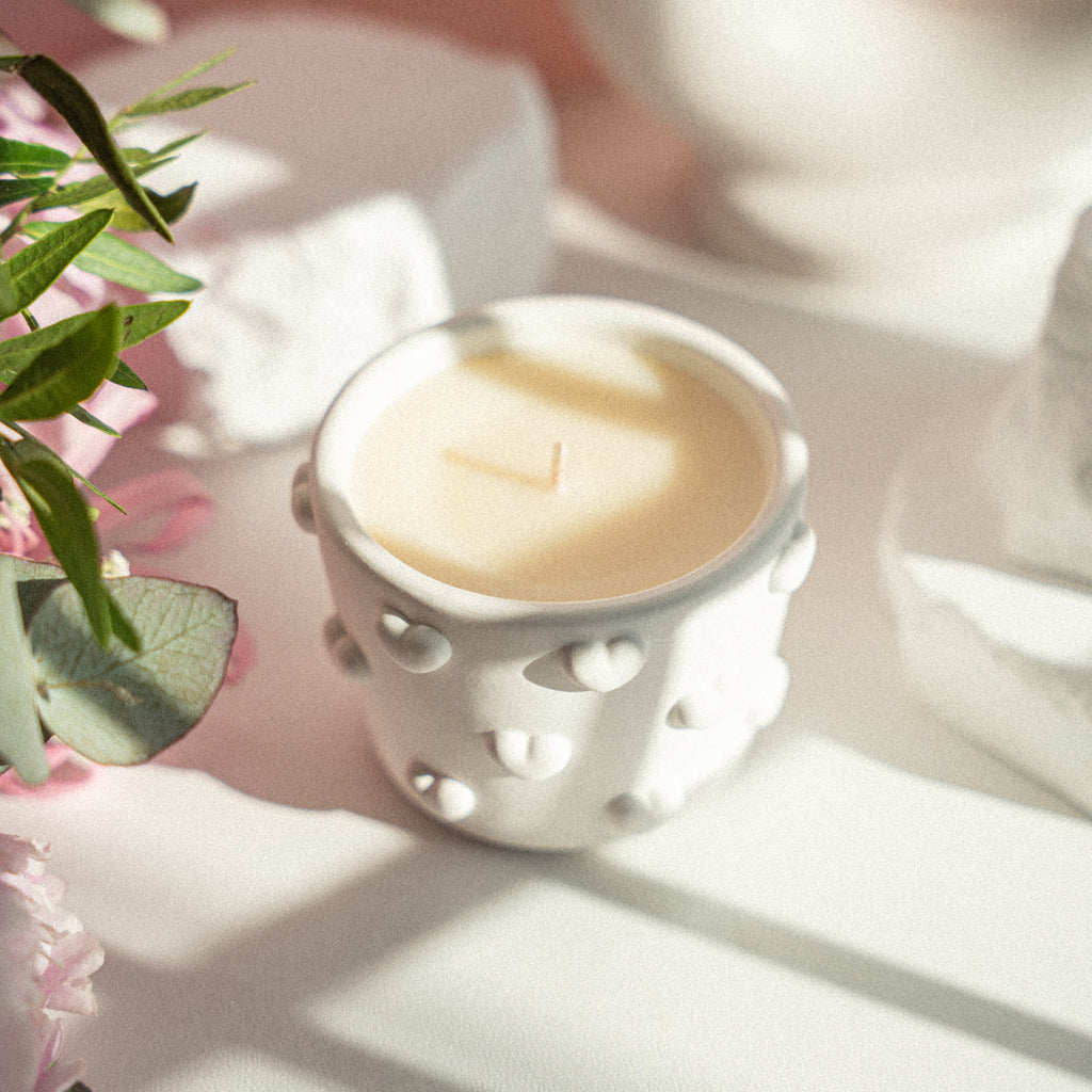 Handmade candle in a white gypsum jar with raised heart design, photographed from the front on a light background