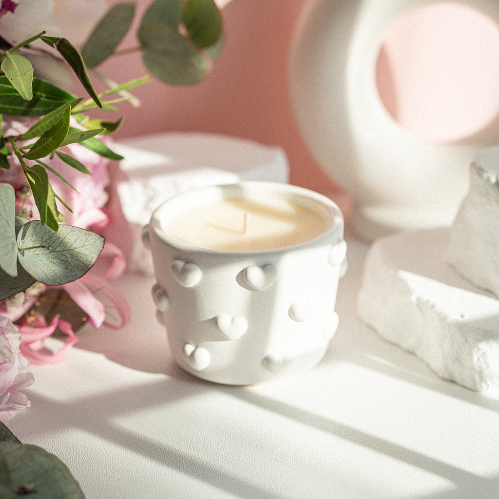 Elegant white gypsum candle jar with decorative hearts, side view showing texture and soft shadows