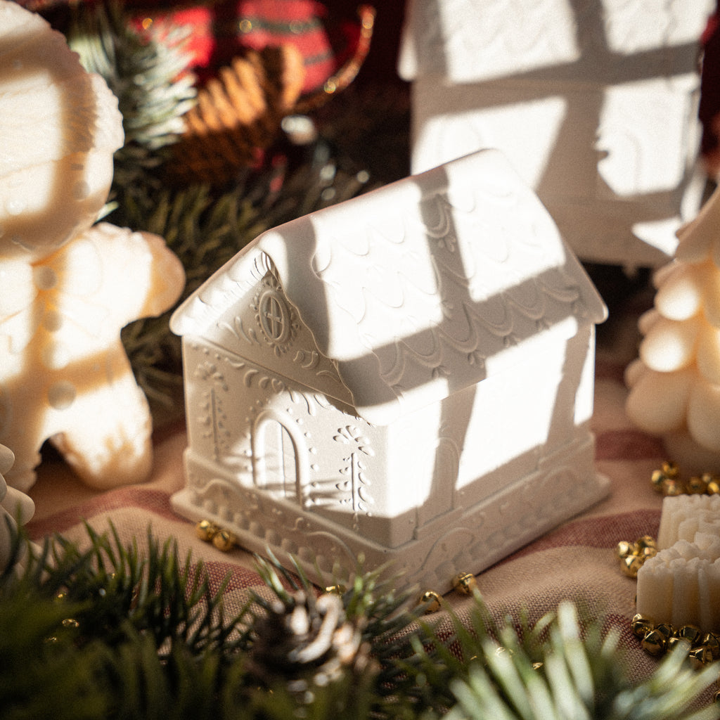White handmade gypsum candle shaped as gingerbread house with intricate details